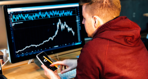 Man checks his phone whilst analysing data on a computer
