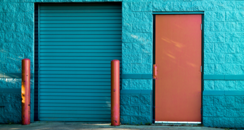 Blue shutters pulled down with bollards next to a door.
