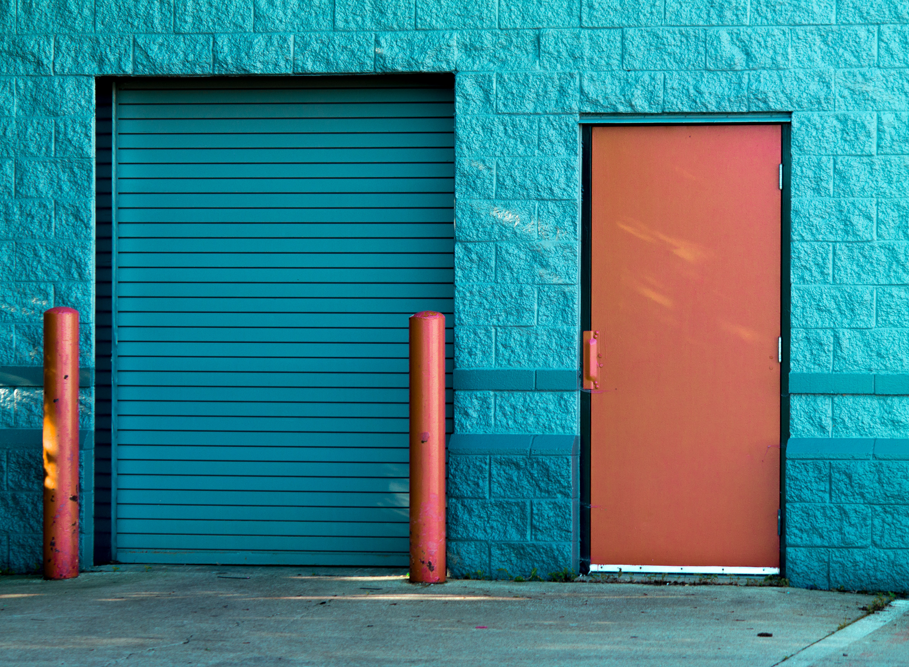 Blue shutters pulled down with bollards next to a door.