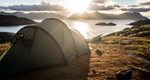 Pitched tent overlooking a view of a loch at sunset