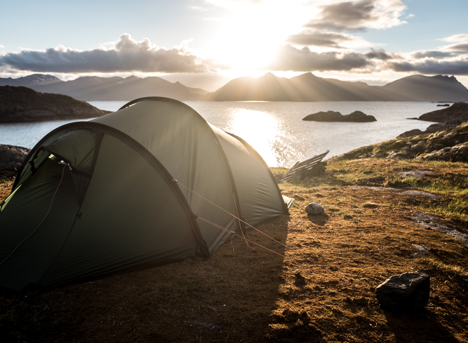 Pitched tent overlooking a view of a loch at sunset