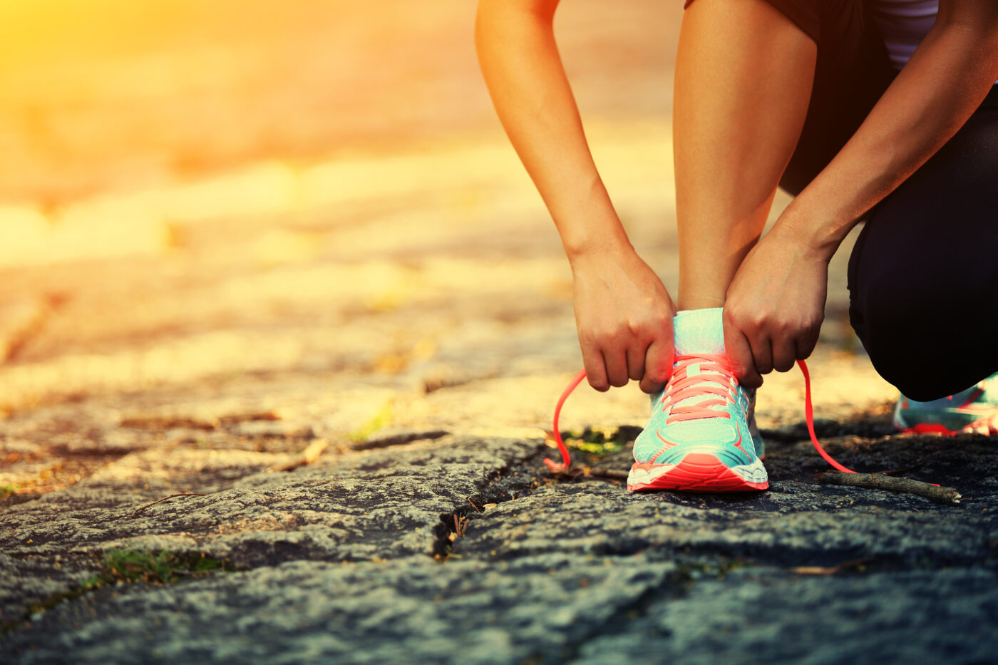 Woman lacing up her running shoes at sunset