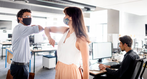 Young businesspeople in protective masks elbow bumping in an office