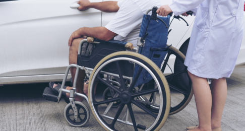 Patient in a wheelchair being helped on a car park