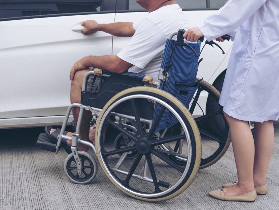 Patient in a wheelchair being helped on a car park